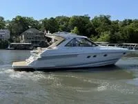 The Image of 2010 Regal 46 Sport Coupe yacht on calm water, with marina and trees in background. - 2