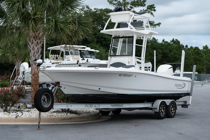 Slide: The Image of 2019 Robalo 246 Cayman SD boat on trailer, parked near palm trees. - 11