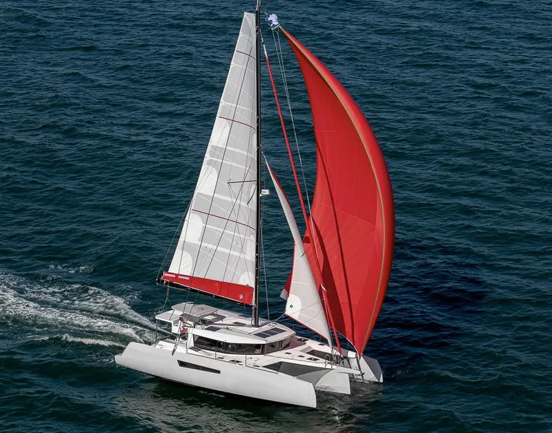 Slide: The Image of 2025 NEEL 47 trimaran sailing with red and white sails on open water. - 2