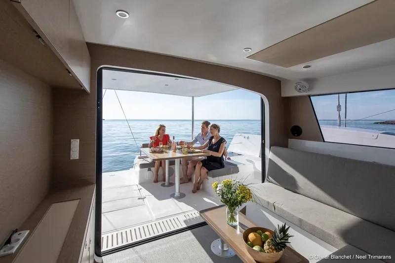 Slide: The Image of Modern NEEL 47 trimaran interior with people dining, ocean view, and elegant decor, 2025 model. - 6