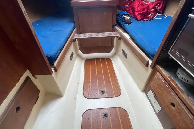 Slide: The Image of Interior of a 1980 Falmouth Cutter sailboat with wooden flooring and blue cushions. - 11