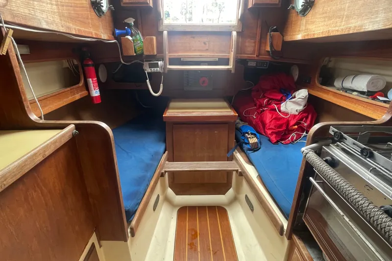 Slide: The Image of Interior of a 1980 Falmouth Cutter sailboat with wooden furnishings and blue cushions. - 12