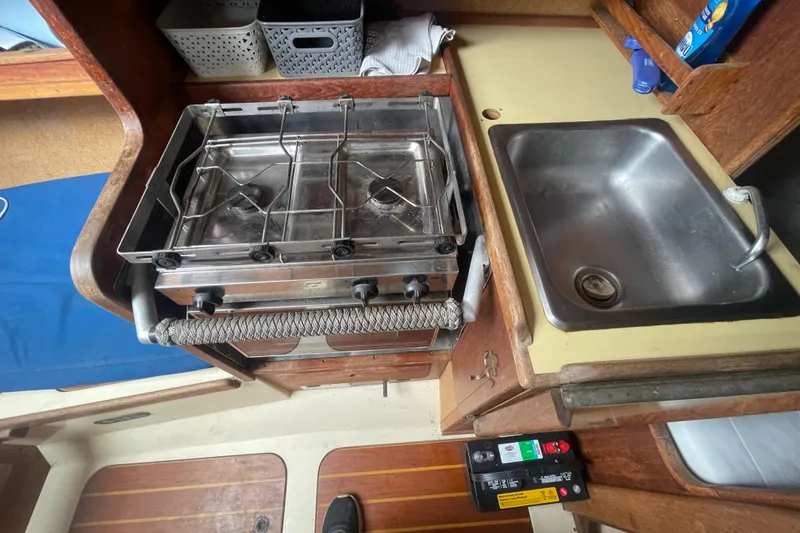 Slide: The Image of 1980 Falmouth Cutter interior with stove and sink in compact kitchen area. - 14