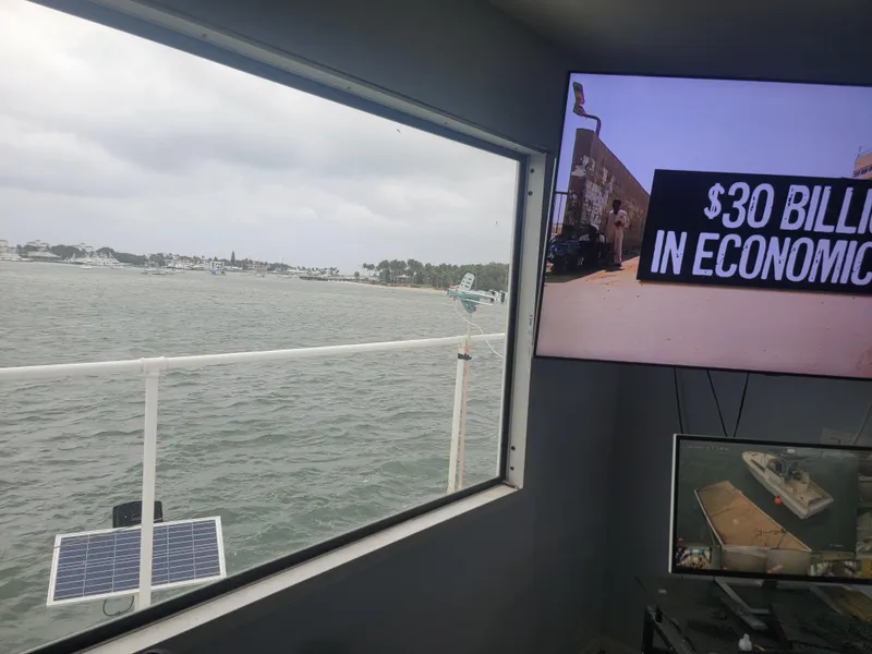 Slide: The Image of Floating home interior with water view, solar panel, and economic news on screens. - 23