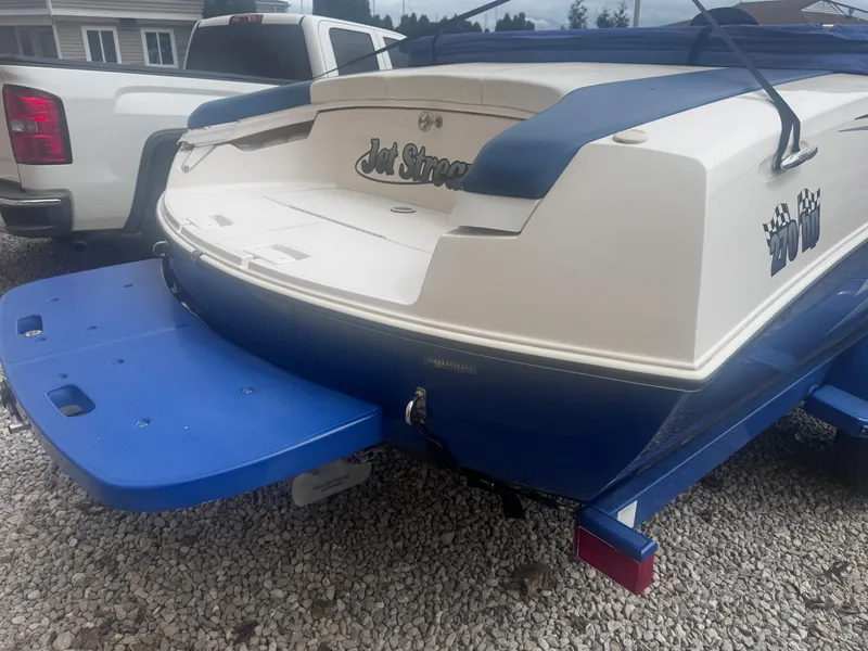 Slide: The Image of 2003 Yamaha Boats 210LX with blue swim platform, parked on gravel. - 2