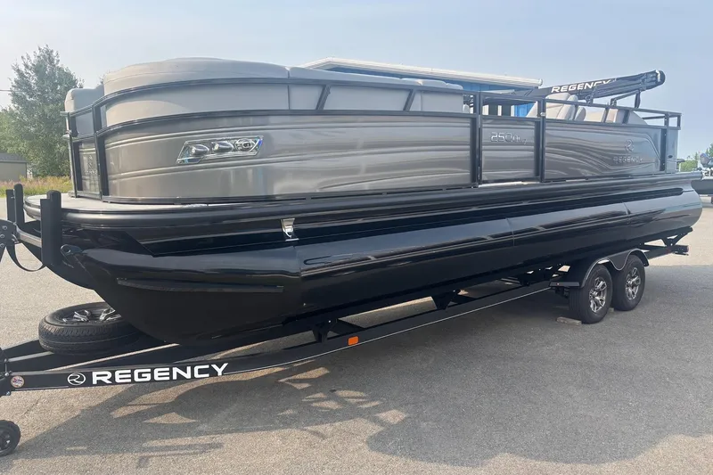 Slide: The Image of 2025 Regency 250 DL3 pontoon boat on trailer, sleek design, parked outdoors. - 0
