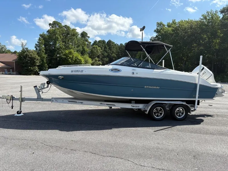 Slide: The Image of 2021 Stingray 231 DC boat on trailer in parking lot, surrounded by trees. - 5