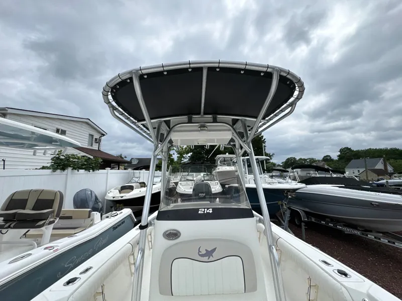 Slide: The Image of 2017 Mako 214 CC boat with T-top, parked among other boats under cloudy skies. - 12