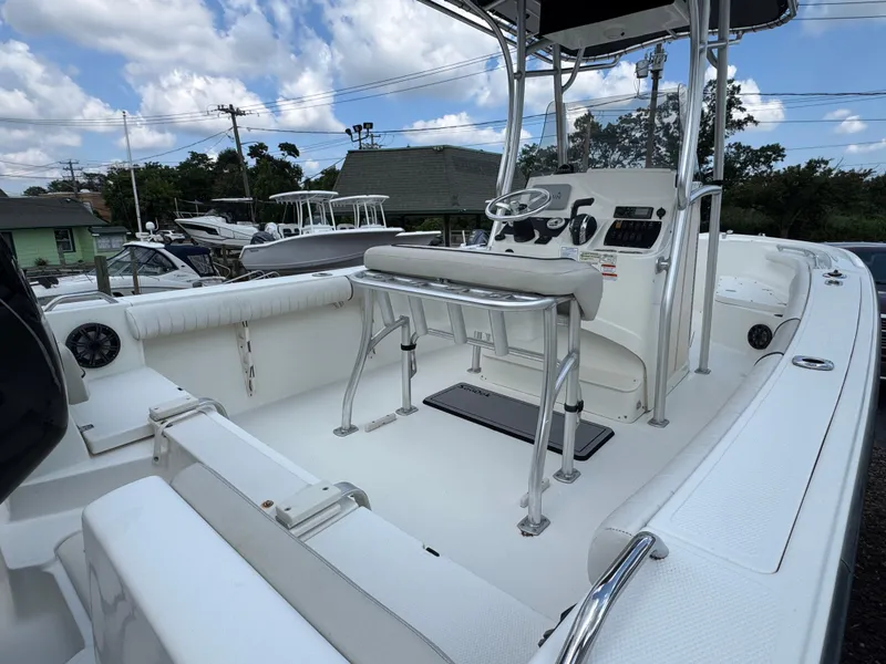 Slide: The Image of 2017 Mako 214 CC boat interior with steering console and seating, under a partly cloudy sky. - 16