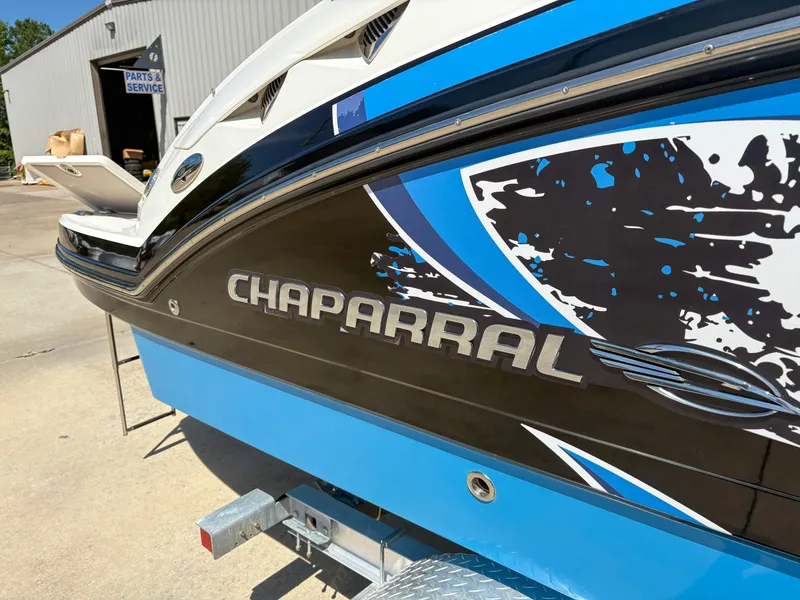 Slide: The Image of 2012 Chaparral 244 Xtreme boat with blue and black design, parked near service area. - 5