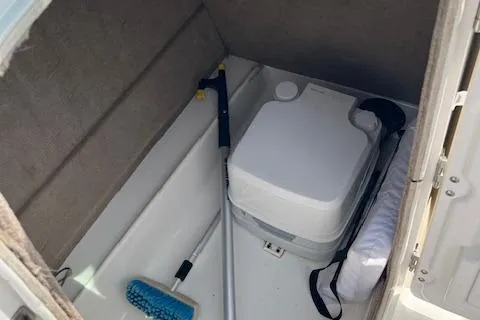 Slide: The Image of 2014 NauticStar 223DC Sport Deck storage area with portable toilet and cleaning tools. - 13