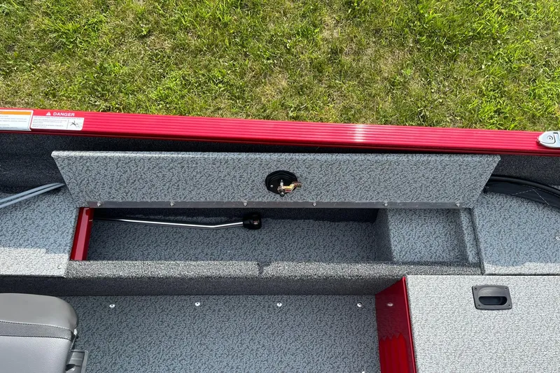 Slide: The Image of 2026 Lund 1650 Angler SS boat interior with storage compartment, red trim, and gray flooring. - 31