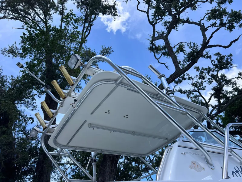 Slide: The Image of 1999 Glacier Bay 2670 Island Runner boat with rod holders, viewed from below against trees and sky. - 11