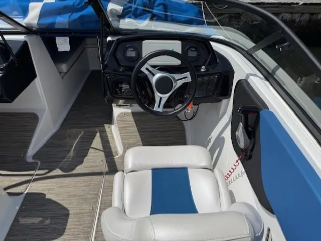 Slide: The Image of 2021 Glastron GX 210 Sport boat interior with steering wheel and blue-accented seating. - 11