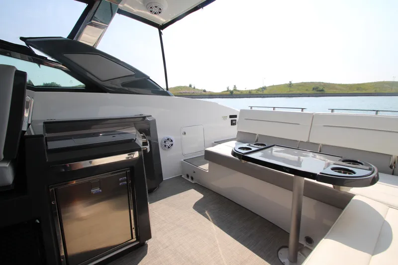 Slide: The Image of 2018 Cobalt A36 boat interior with seating, table, and mini-fridge, near water. - 23