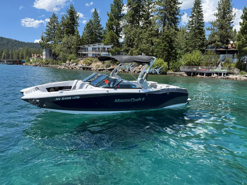 Slide: The Image of 2021 MasterCraft X24 boat on clear blue lake with forested shoreline. - 2