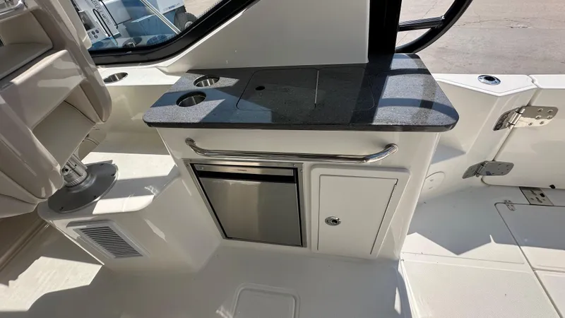 Slide: The Image of 2026 Boston Whaler 325 Conquest interior with kitchenette, featuring countertop, storage, and seating. - 25
