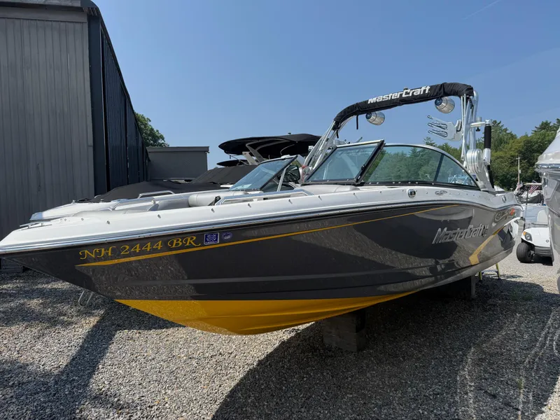 Slide: The Image of 2015 MasterCraft X10 boat with sleek design, parked on gravel near a building. - 1