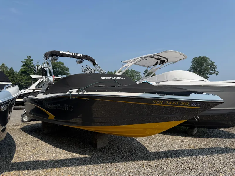 Slide: The Image of 2015 MasterCraft X10 boat with cover, parked on gravel, surrounded by other boats. - 3