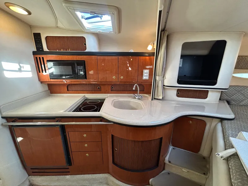 Slide: The Image of 2001 Sea Ray 310 Sundancer galley with wood cabinetry, sink, microwave, and cooktop. - 6