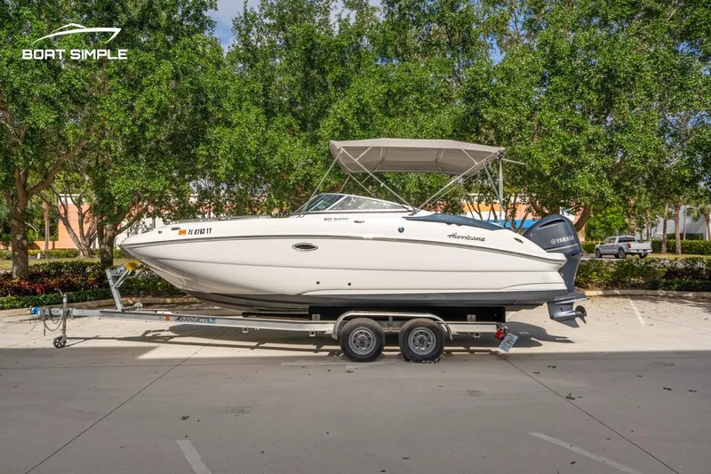 Slide: The Image of 2025 Hurricane SunDeck 2400 OB boat on trailer, parked outdoors with trees in background. - 0