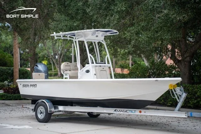 Slide: The Image of 2024 Sea Pro 208 Bay boat on trailer, parked outdoors, surrounded by trees. - 2