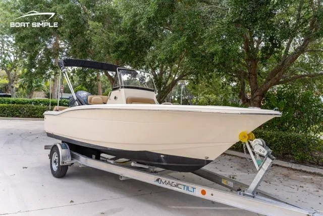 Slide: The Image of 2024 Scout 195 Sportfish boat on trailer, parked outdoors with trees in background. - 2