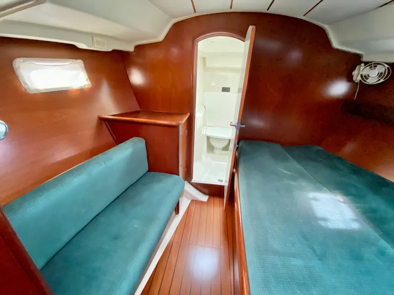 Slide: The Image of 1999 Beneteau 411 yacht cabin with wooden interior, teal seating, and visible bathroom. - 30