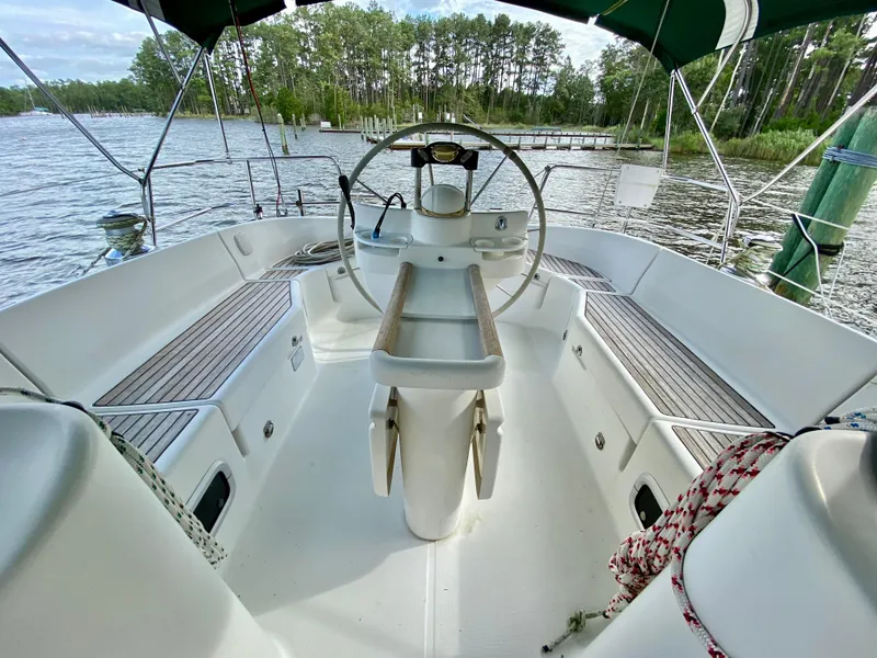 Slide: The Image of Cockpit of 1999 Beneteau 411 sailboat with wooden seating and steering wheel, docked by a forested shoreline. - 7