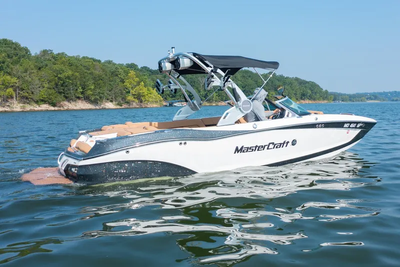 Slide: The Image of 2021 MasterCraft X22 boat cruising on a scenic lake with lush green shoreline. - 0