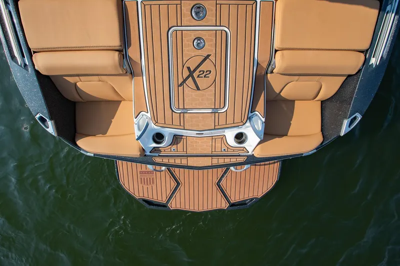 Slide: The Image of 2021 MasterCraft X22 boat deck with tan seating and wood finish, viewed from above. - 13