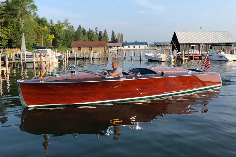 The Image of Vintage 1931 Hacker-Craft 26 Dolphin boat on a serene lake near docks and boathouses. - 0