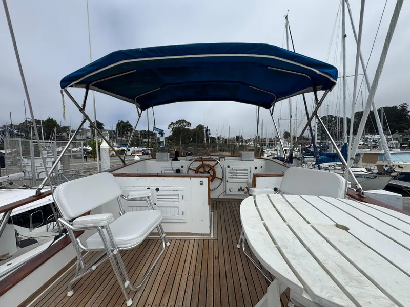 Slide: The Image of 1984 Monk 36 Trawler with blue canopy, white seating, and wooden deck in marina. - 2
