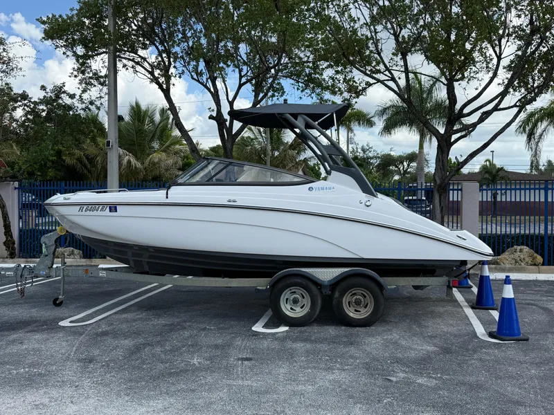 Slide: The Image of 2017 Yamaha Boats 212 Limited S on trailer, parked outdoors with trees in background. - 10