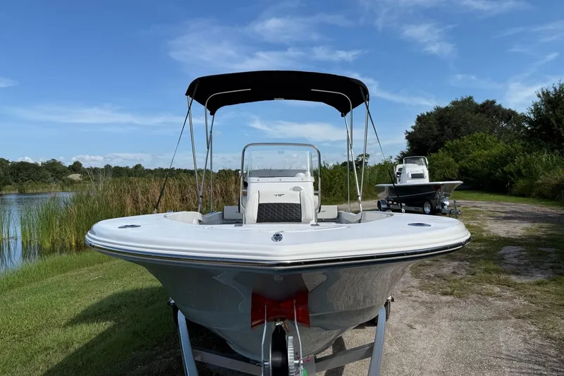 Slide: The Image of 2026 Tidewater 180 CC Adventure boat on trailer by a lake under blue sky. - 13