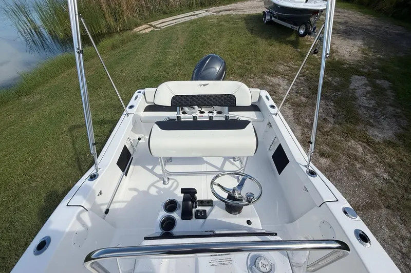 Slide: The Image of 2026 Tidewater 180 CC Adventure boat interior with steering wheel and seating, near grassy shoreline. - 20
