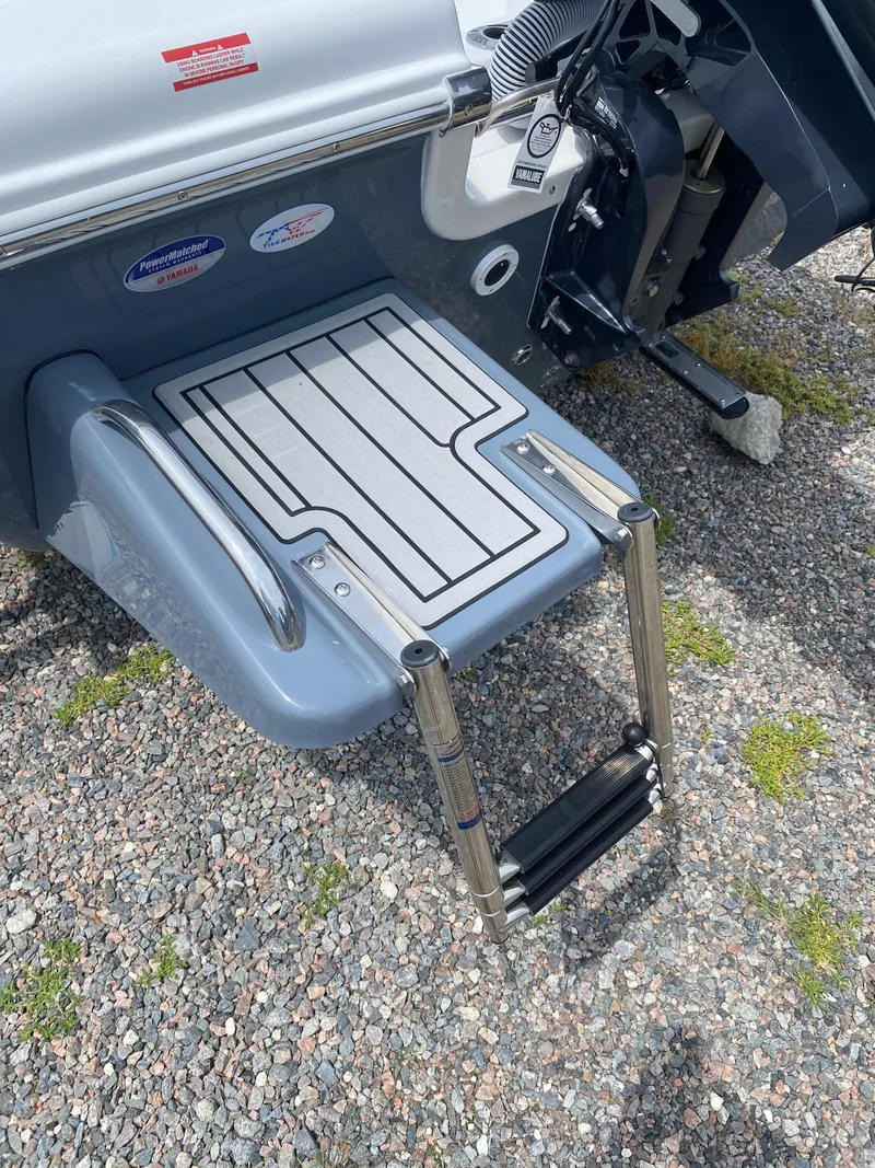 Slide: The Image of 2026 Tidewater 180 CC Adventure boat swim platform with ladder on gravel surface. - 12
