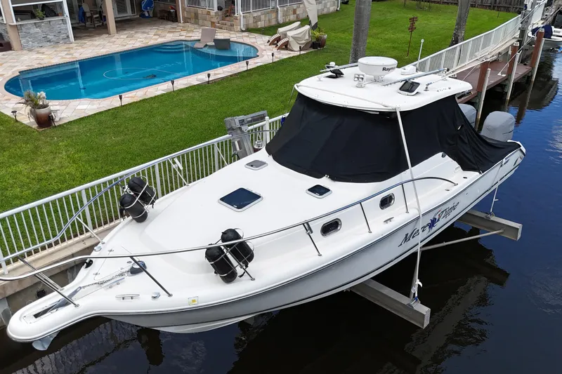 Slide: The Image of 2007 Pursuit OS 335 Offshore boat docked near a house, covered with a black tarp. - 3