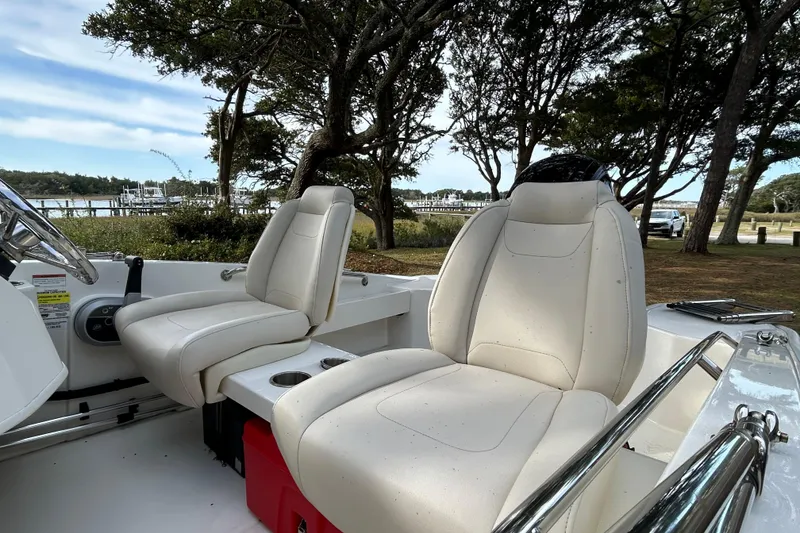 Slide: The Image of 2023 Boston Whaler 160 Super Sport interior with white seats, parked near a scenic waterfront. - 17