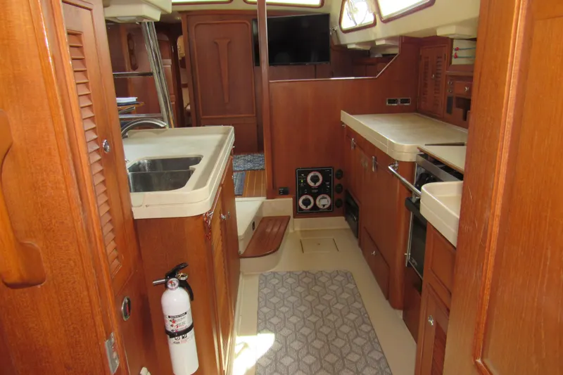Slide: The Image of Interior of 2003 Island Packet 485 yacht, featuring a well-equipped kitchen and wooden cabinetry. - 20