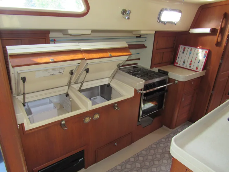 Slide: The Image of 2003 Island Packet 485 yacht kitchen with open storage, stove, and wooden cabinetry. - 21