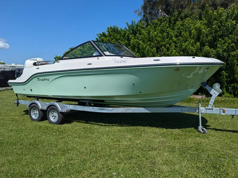 The Image of 2026 Bayliner Trophy T22SC boat on trailer, parked on grass with trees in background. - 0