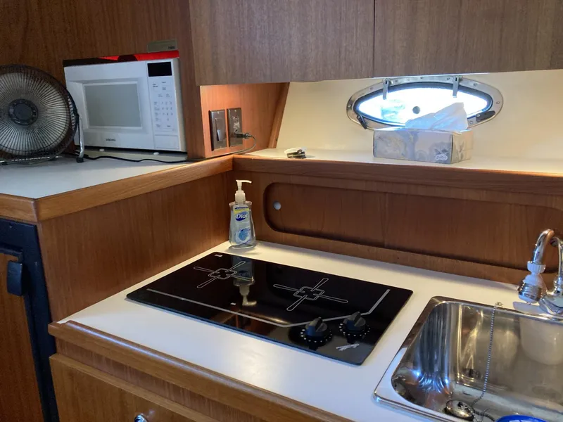 Slide: The Image of Compact kitchen area in a 2000 Tiara Yachts 3100 Open, featuring a stove, sink, and microwave. - 17