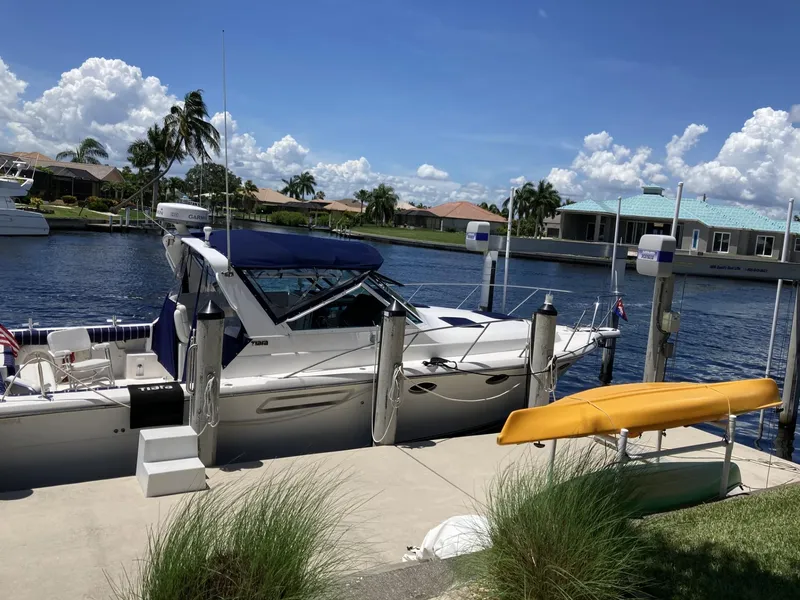 Slide: The Image of 2000 Tiara Yachts 3100 Open docked by a waterfront home under a clear blue sky. - 3