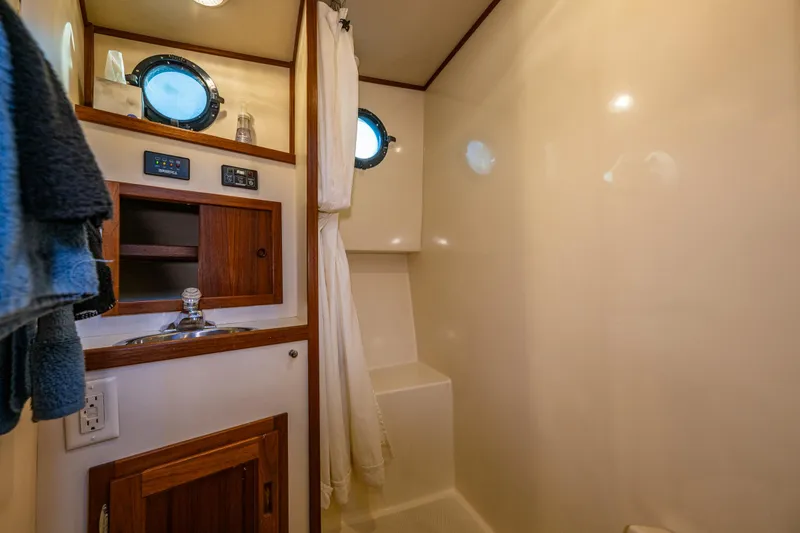 Slide: The Image of Bathroom interior of a 2000 Nordic Tug 32, featuring a sink, portholes, and wooden cabinetry. - 20