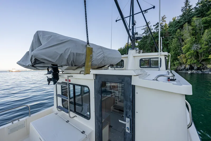 Slide: The Image of Nordic Tug 32 boat, 2000 model, docked near forested shoreline, covered equipment on deck. - 27