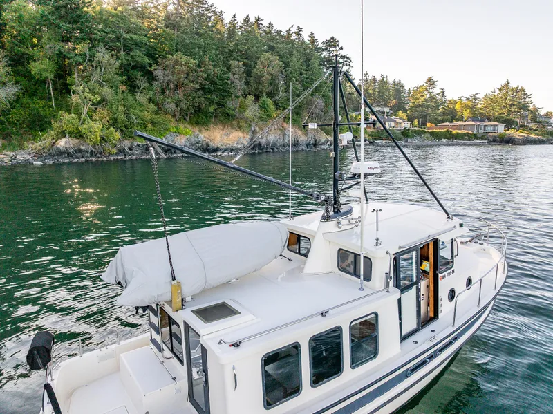 Slide: The Image of Nordic Tug 32 (2000) cruising near a forested shoreline, showcasing its classic design and features. - 28