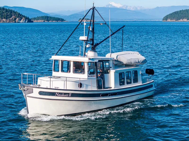 Slide: The Image of Nordic Tug 32 boat cruising on blue water, scenic mountain backdrop, 2000 model. - 34