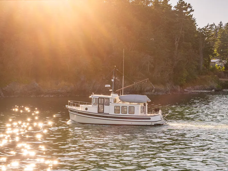Slide: The Image of Nordic Tug 32 boat cruising on sunlit water near forested shoreline, 2000 model. - 36