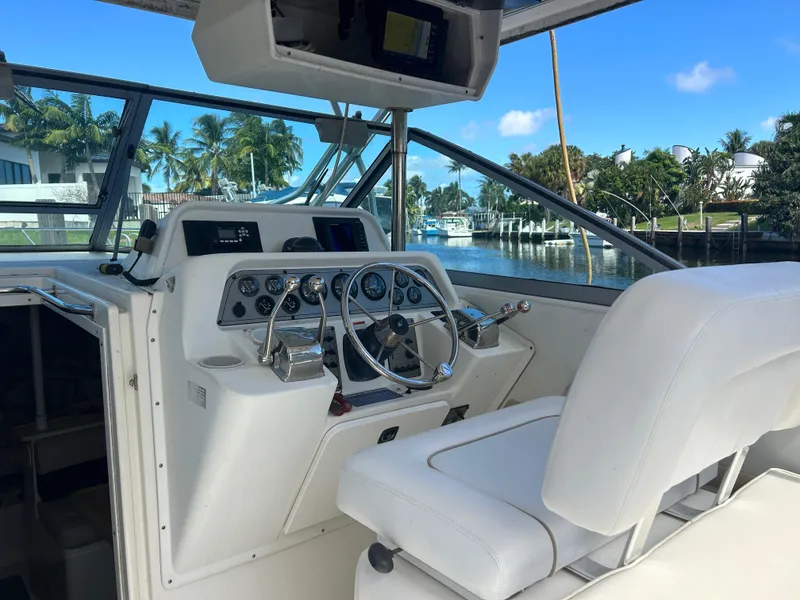 Slide: The Image of 1999 Wellcraft 330 Coastal helm with white seating, docked near palm trees and waterfront homes. - 14